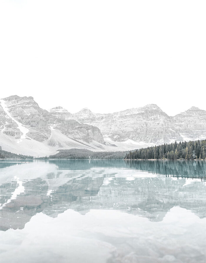 product-image-11-14 A still Mountain Lake reflects pine trees and snow-capped mountains under a bright, overcast sky. Nature and landscape poster print available in A1 to A4 sizes.