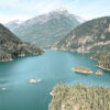 A large blue mountain lake surrounded by forested mountains, with several small tree-covered islands visible in the water under a mostly clear sky. Nature and landscape poster print available in A1 to A4 sizes.