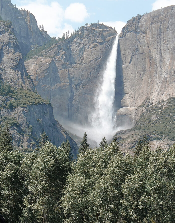 product-image-11-14 A tall mountain waterfall cascades down a rocky cliff surrounded by trees, with a clear blue sky above. Nature and landscape poster print available in A1 to A4 sizes.