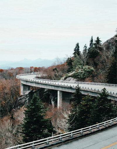 A curved Mountain Road winds through a forested, hilly landscape with autumn foliage and evergreen trees beneath an overcast sky. Nature and landscape poster print available in A1 to A4 sizes.