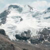 Snow-capped mountain peak with exposed rock faces and glaciers under a partly cloudy sky. Nature and landscape poster print available in A1 to A4 sizes.