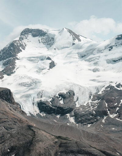 Snow-capped mountain peak with exposed rock faces and glaciers under a partly cloudy sky. Nature and landscape poster print available in A1 to A4 sizes.