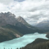 A turquoise mountain lake is surrounded by dense evergreen forest and rugged mountains under a cloudy sky. Nature and landscape poster print available in A1 to A4 sizes.