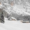 A snow-covered mountain lodge stands among pine trees with large, rocky mountains in the background under a cloudy sky. Nature and landscape poster print available in A1 to A4 sizes.