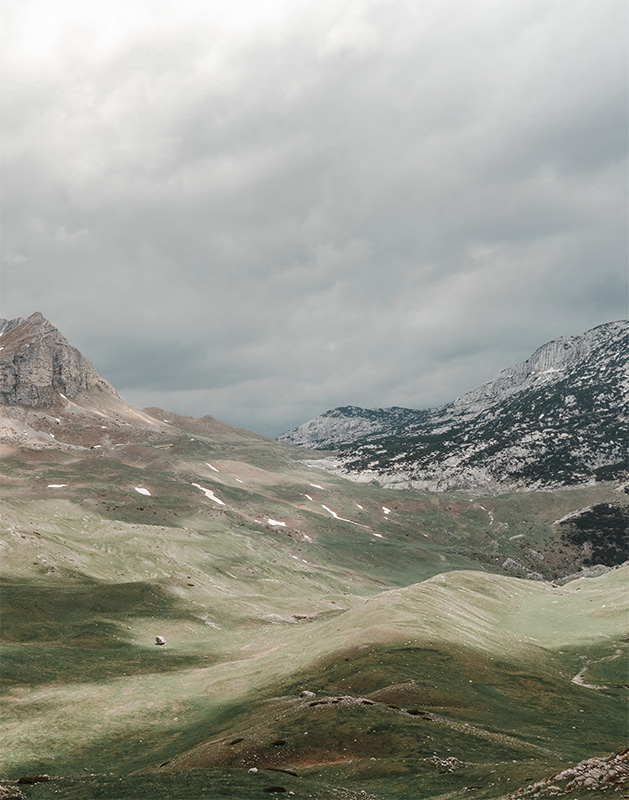 A wide, grassy valley with rolling foothills and rocky mountains beneath a cloudy sky. Nature and landscape poster print available in A1 to A4 sizes.