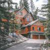 A large Forest Lodge-style wooden cabin with stone accents sits among pine trees, featuring a sloped driveway, balconies, and multiple windows. Nature and landscape poster print available in A1 to A4 sizes.