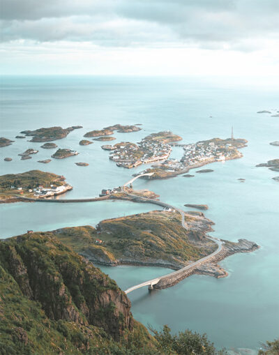 A coastal landscape in Norway, featuring the Lofoten Islands with small islets connected by winding roads and bridges, surrounded by a calm blue sea under a partly cloudy sky. Nature and landscape poster print available in A1 to A4 sizes.