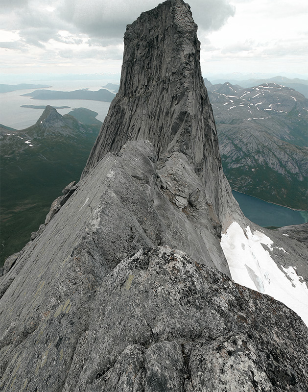 product-image A sharp, rocky mountain ridge with a steep Mountain Peak, surrounded by distant mountains, patches of snow, and a lake below under a cloudy sky. Nature and landscape poster print available in A1 to A4 sizes.