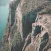 Aerial view of Preikestolen, a flat-topped cliff with people standing on it, overlooking a fjord and steep rocky landscape in Norway. Nature and landscape poster print available in A1 to A4 sizes.