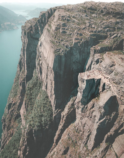 Aerial view of Preikestolen, a flat-topped cliff with people standing on it, overlooking a fjord and steep rocky landscape in Norway. Nature and landscape poster print available in A1 to A4 sizes.