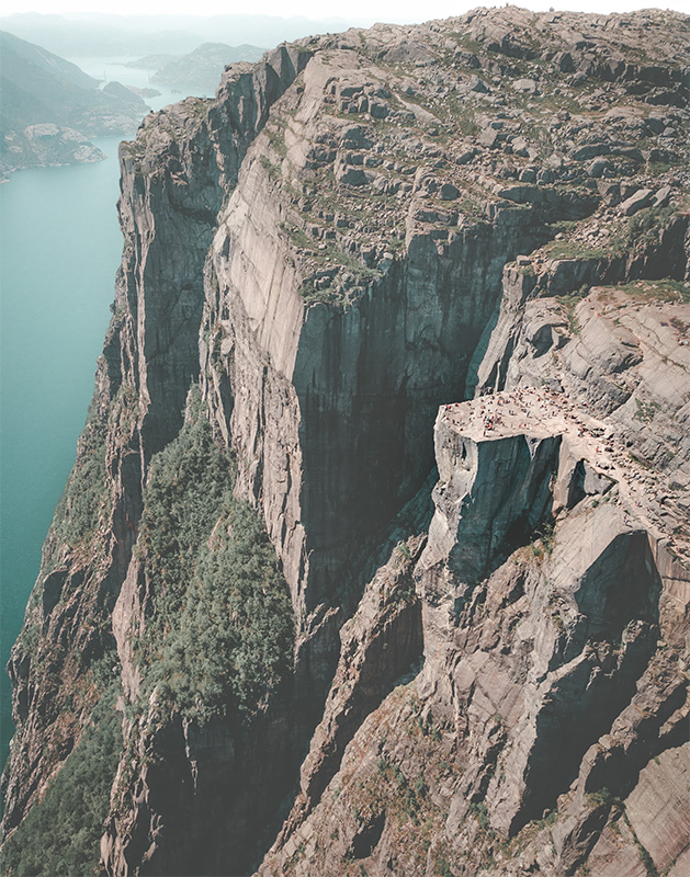 product-image Aerial view of Preikestolen, a flat-topped cliff with people standing on it, overlooking a fjord and steep rocky landscape in Norway. Nature and landscape poster print available in A1 to A4 sizes.