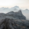 Rocky mountain peaks layered in mist create a stunning mountainscape, with a hazy sky and distant jagged ridges fading into the background. Nature and landscape poster print available in A1 to A4 sizes.