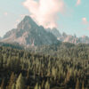 The dramatic Mountain Range 3 features jagged peaks soaring above a dense forest of evergreen trees beneath a partly cloudy sky. Nature and landscape poster print available in A1 to A4 sizes.