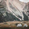 A person stands on grassy terrain with scattered rocks, surrounded by steep, forested mountains under a cloudy sky. Nature and landscape poster print available in A1 to A4 sizes.