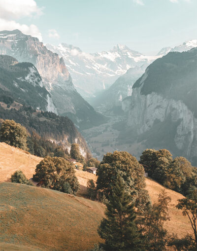 A scenic mountain valley with green hills, scattered trees, and towering cliffs under a partly cloudy sky. Nature and landscape poster print available in A1 to A4 sizes.