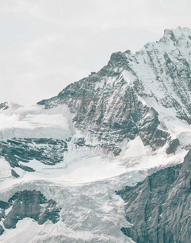 Snow-covered mountain peak with rocky, jagged ridges and patches of ice under a cloudy sky. Nature and landscape poster print available in A1 to A4 sizes.