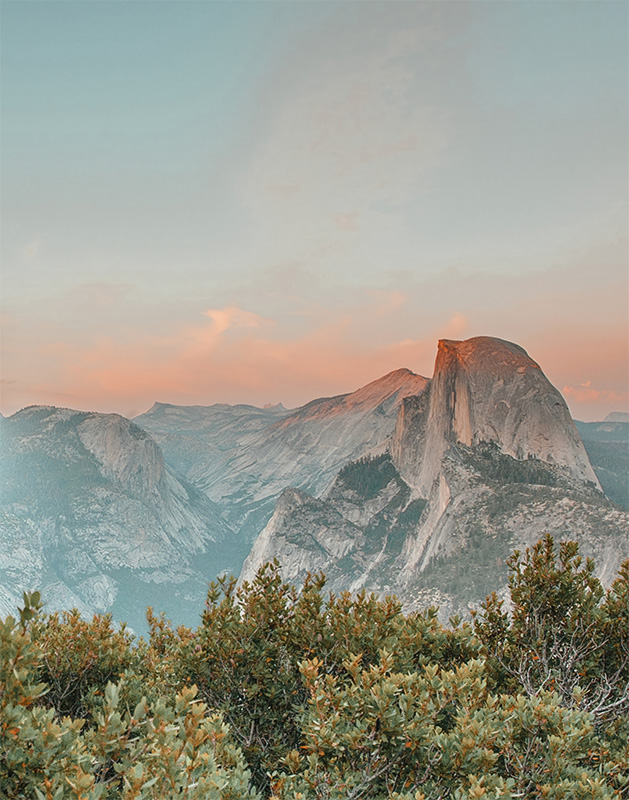 product-image View of Half Dome rock formation in Yosemite National Park at sunset, with green shrubs in the foreground and pink clouds in the sky. Nature and landscape poster print available in A1 to A4 sizes.