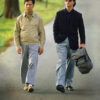 Two men walk side by side on a tree-lined road in this iconic scene from the 1988 movie Rain Man; one wears a tan jacket and beige pants, the other sunglasses, a dark jacket, and carries a grey bag. The text reads Rain Man. Movie poster print available in A1 to A4 sizes.
