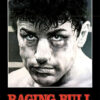 A grayscale close-up of a sweaty boxer’s intense face is shown above the bold red title Raging Bull on a black background, capturing the raw emotion of the iconic 1980 movie. Movie poster print available in A1 to A4 sizes.