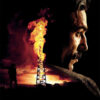 A man’s face in profile is blended with an image of an oil derrick on fire at sunset; a silhouetted figure stands nearby. Text reads, There Will Be Blood, referencing the acclaimed 2007 movie. Movie poster print available in A1 to A4 sizes.