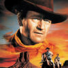 Movie poster for The Searchers (1956) featuring a large portrait of a cowboy in a hat, with two men on horseback riding across a desert landscape at sunset. Movie poster print available in A1 to A4 sizes.
