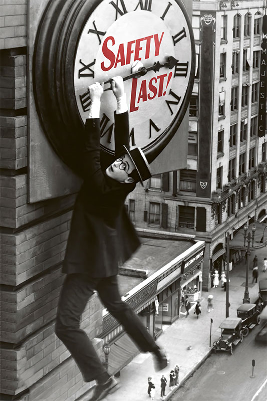 Product-Image_0001_Safety Last!.jpg A man in a suit and hat hangs from the hands of a large clock on a building above a city street, recreating Harold Lloyd’s iconic scene from the silent comedy classic, Safety Last!. Movie poster print available in A1 to A4 sizes.