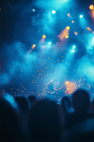 Blue and yellow stage lights shine on musicians performing at a concert, with a blurred crowd in the foreground—perfect for a customizable gig poster or rock band poster. Add your own text to make it uniquely yours! A1 to A4 print sizes.